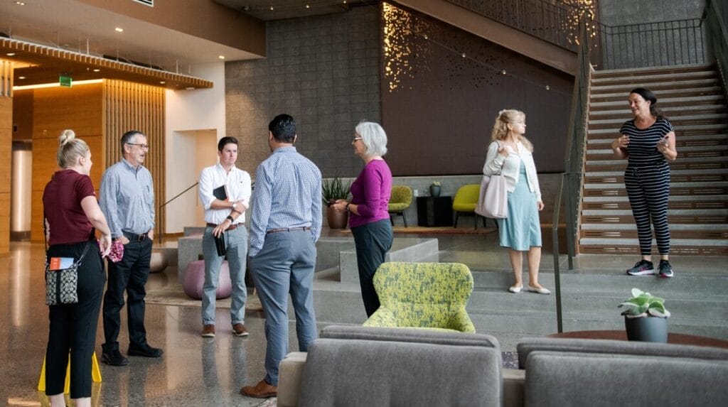 Seven people in the lobby of a professional building, engaged in conversation, with a staircase in the background.