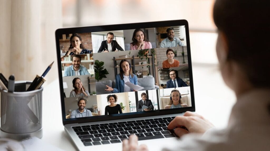 A person looking at their laptop screen with multiple team members shown during a virtual meeting.

