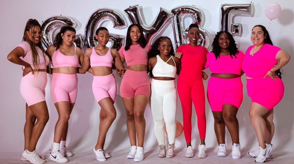 Eight people wearing athletic clothing and standing in front of balloons that spell out “GGYBF.”
