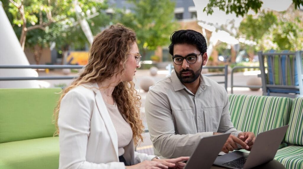 Two professional colleagues sitting outdoors with their laptops