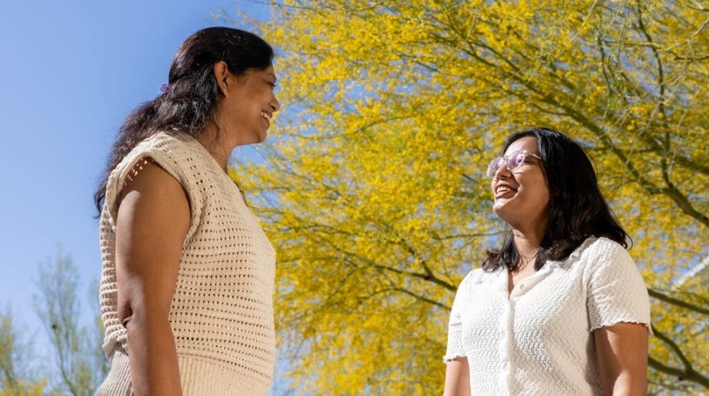 Two people standing outside smiling and talking to each other.