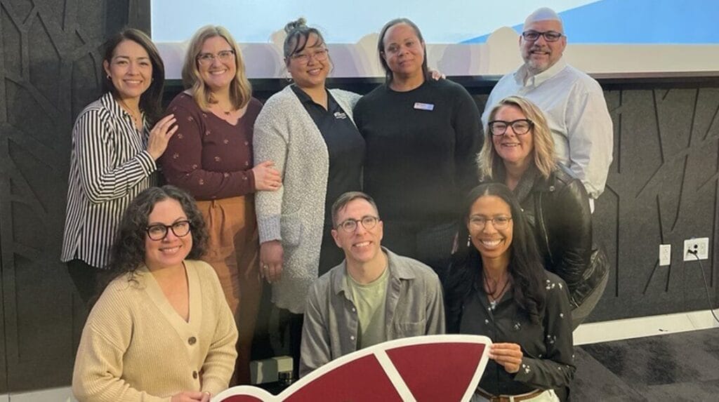 Nine people smile at the camera at a community event and hold a rocket cutout.