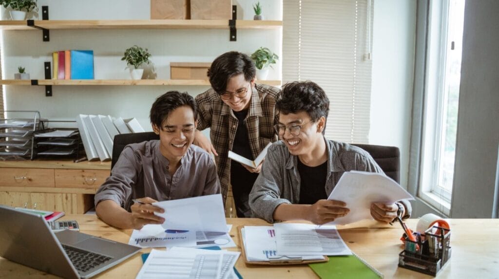 Three people sitting at a large table looking at paperwork