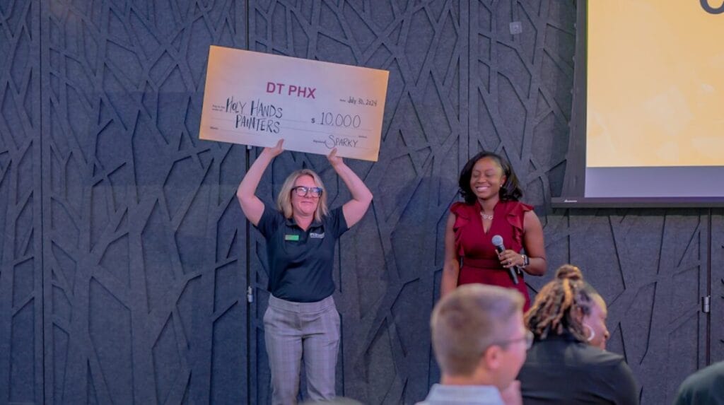 A person holding an oversized check at an event and another person is holding a microphone.