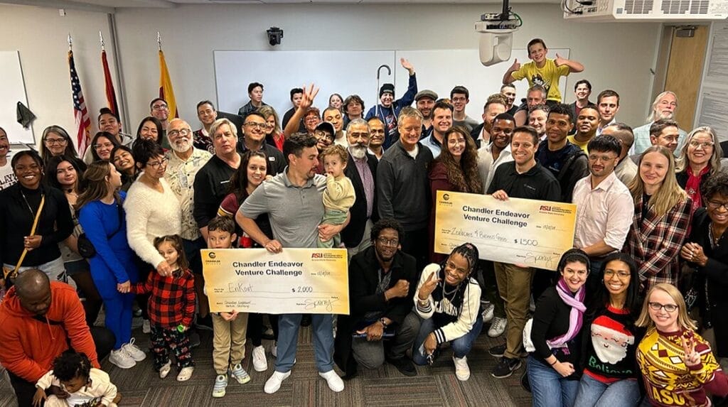 A group of people smiling at the camera at an entrepreneurial event with two people holding large checks