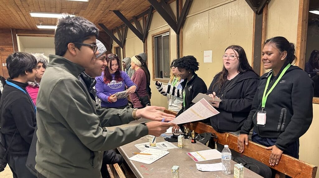  A group of students standing at a table and helping each other check in for an event at a camp 