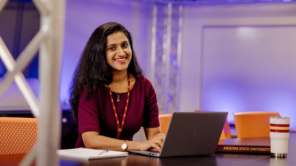 A person sitting at a table working on their laptop with a notebook and coffee on the table