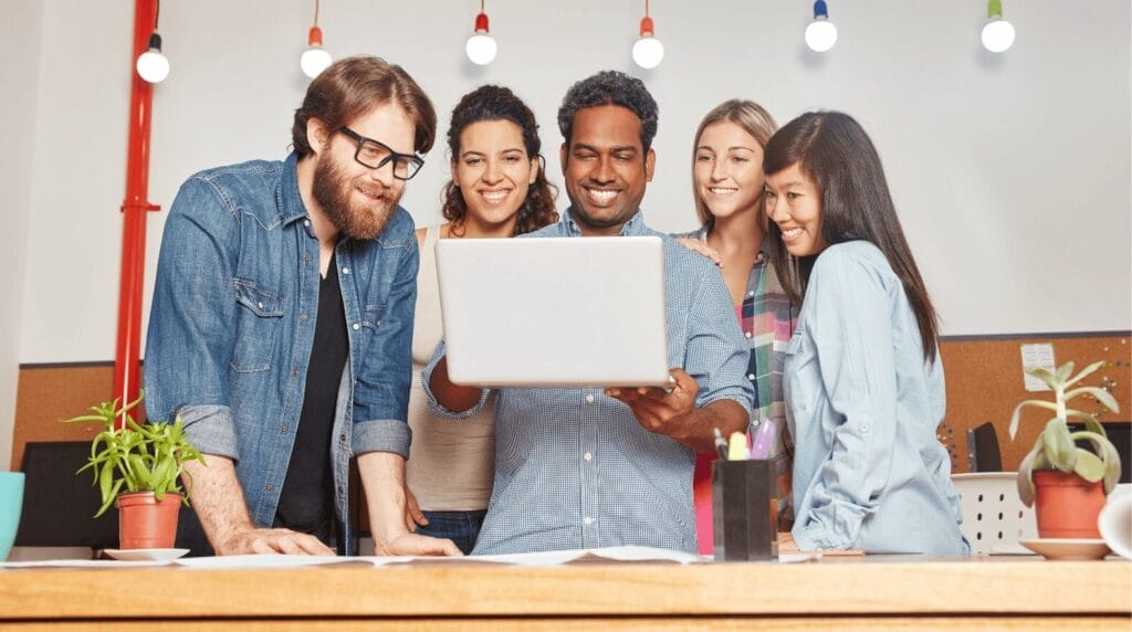 Five coworkers looking at a laptop at a desk