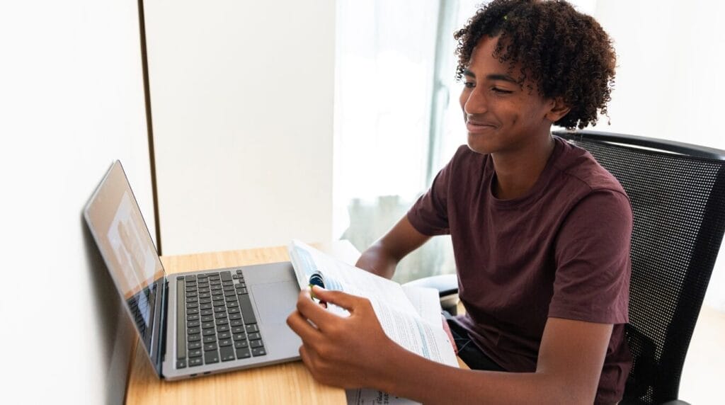 Teenager seated at a desk, focused on his laptop while attending an online class.
