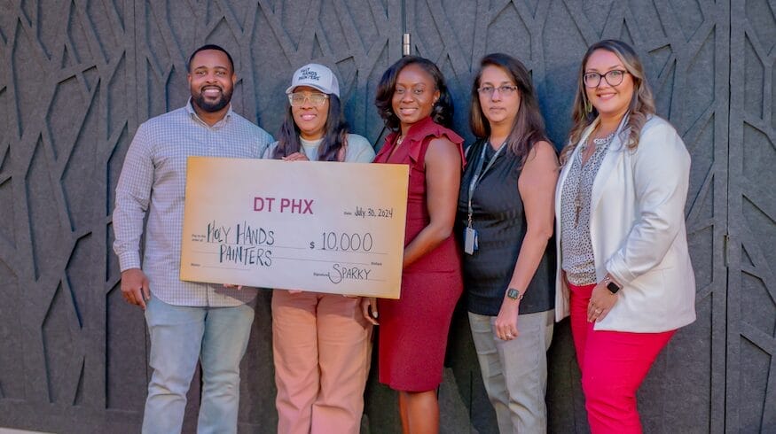 Five people holding a large check at a community startup event.
