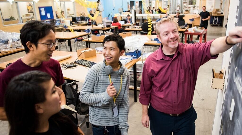 Three university students work with a professor in a classroom