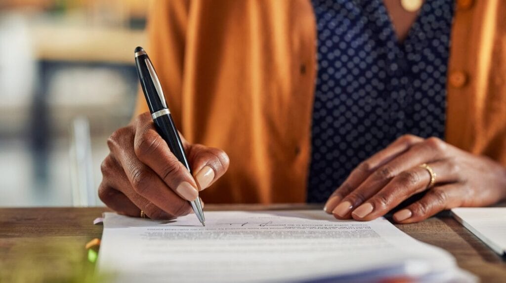 A view of a person’s hands signing a document on a desk.