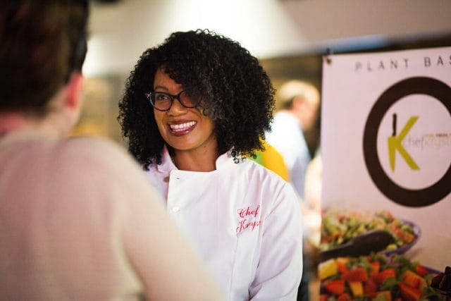 Woman wearing glasses and chef coat, smiling at another person