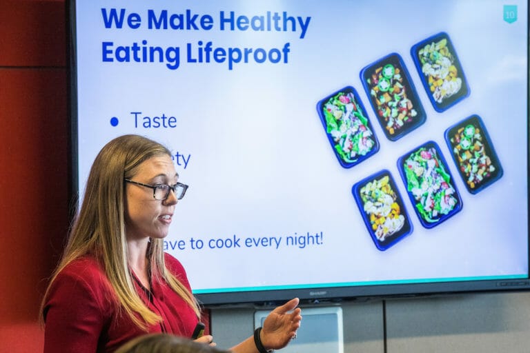 Woman giving a presentation, standing in front of a large screen with images of food