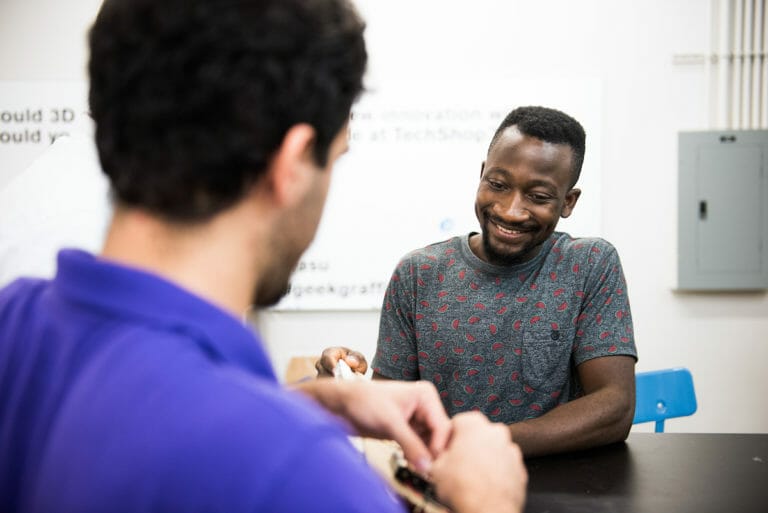 Two men sitting at a table, you can see one man's face and the back of the other man's head