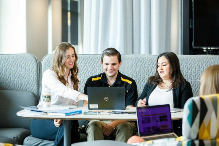 Three people, two women and one man, sitting at a table looking at a computer.