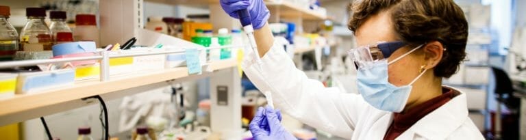 An ASU researcher wearing a mask and safety goggles conducts an experiment using a test tube.