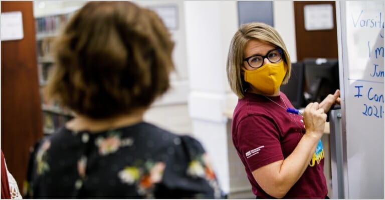 lady wearing a mask writing on a white board