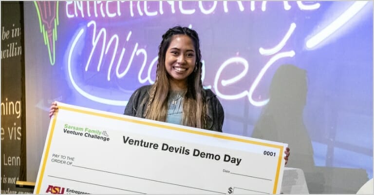 Girl standing on stage holding a large check