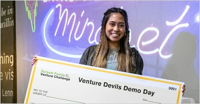 Girl standing on stage holding a large check