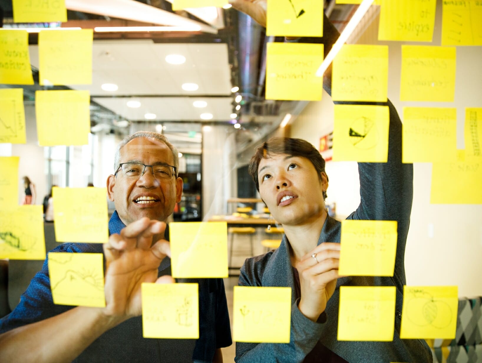 people sticking sticky notes on a glass board