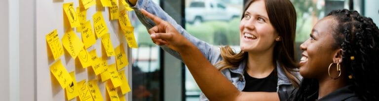 Two ASU students ideate using yellow Post-it notes with words such as “customer,” “problem solver” and “feedback.”