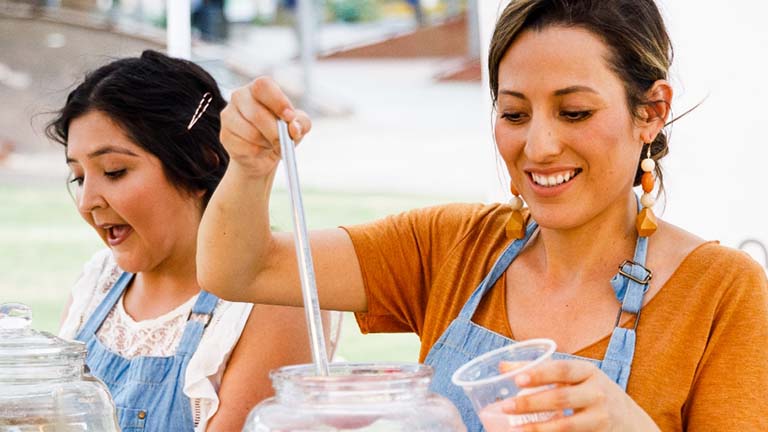 Two women work at their mobile food business serving handcrafted aguas frescas.