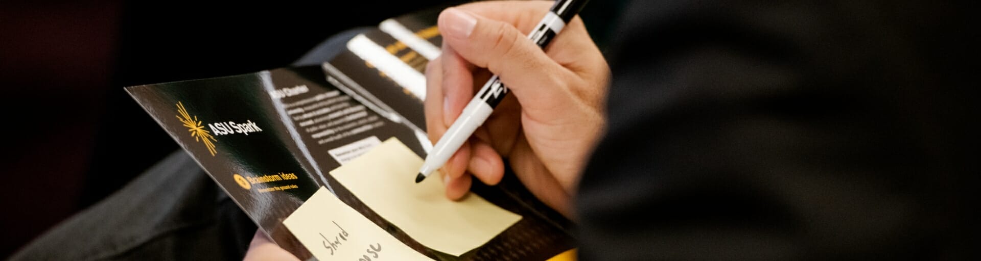 An entrepreneur takes notes on a program using Post-it notes and a black felt-tip marking pen.